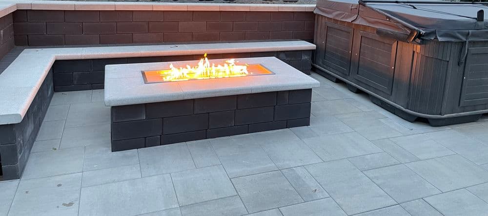 Modern outdoor patio with a fire pit, seating area, and hot tub. Elegant stone design.