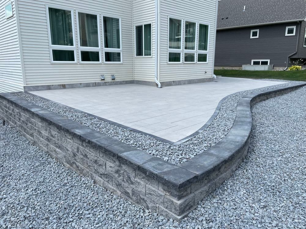 Modern patio with stone edging and gravel landscaping near a residential home.