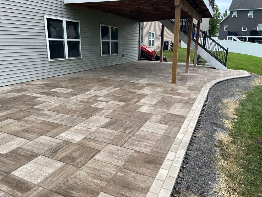 Patio with patterned stone tiles under a covered porch, featuring a landscaped edge.