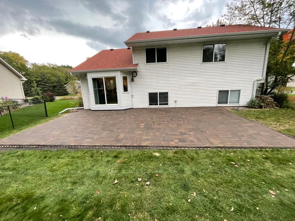 Newly installed paver patio behind a modern white house with a red roof and green lawn.