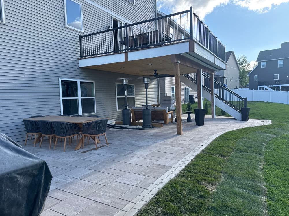 Backyard patio with dining set, outdoor furniture, and elevated deck under blue sky.