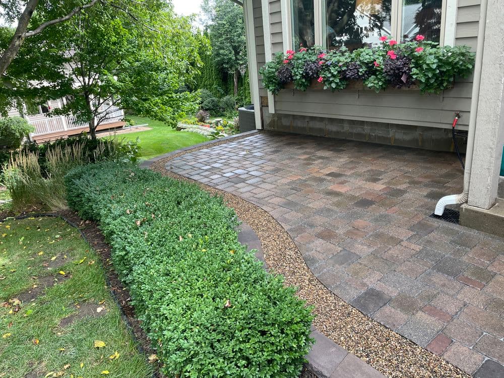 Elegant patio with interlocking pavers, lush greenery, and vibrant flower planters.
