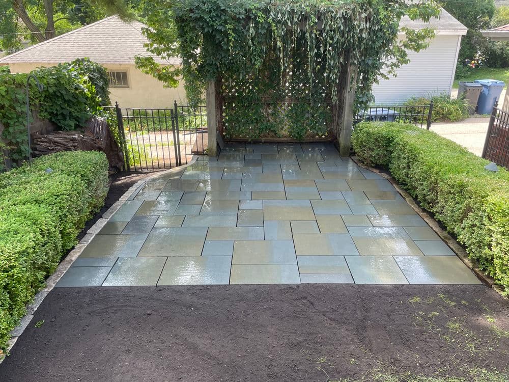 Newly laid blue stone patio with lush greenery and decorative fence in a residential yard.