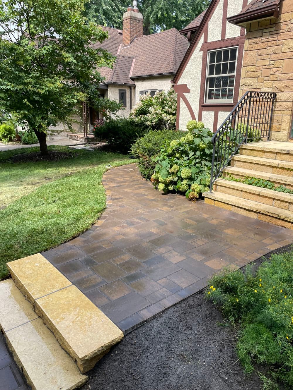 Curved stone pathway leading to a home entrance with landscaped steps and greenery.