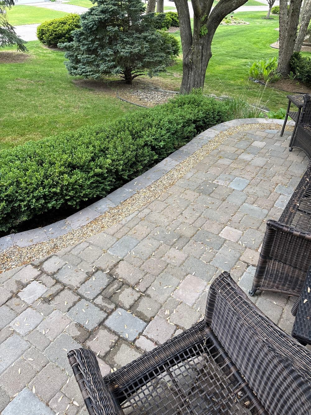 Paved patio area with wicker chairs and lush green landscape in the background.