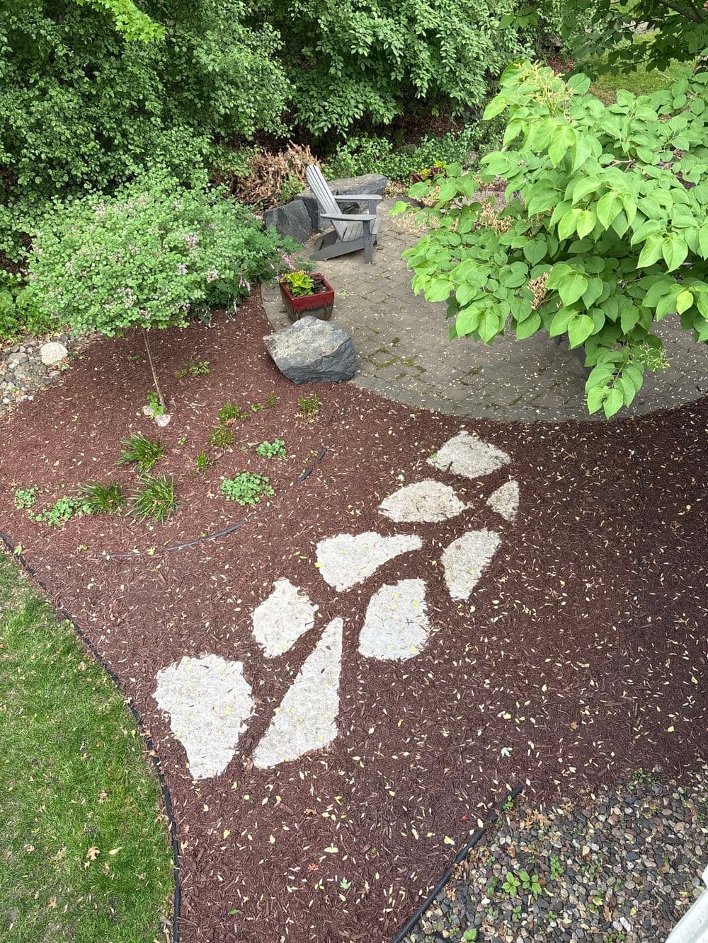 Backyard landscape with stone path, garden, and hardwood seating area surrounded by greenery.