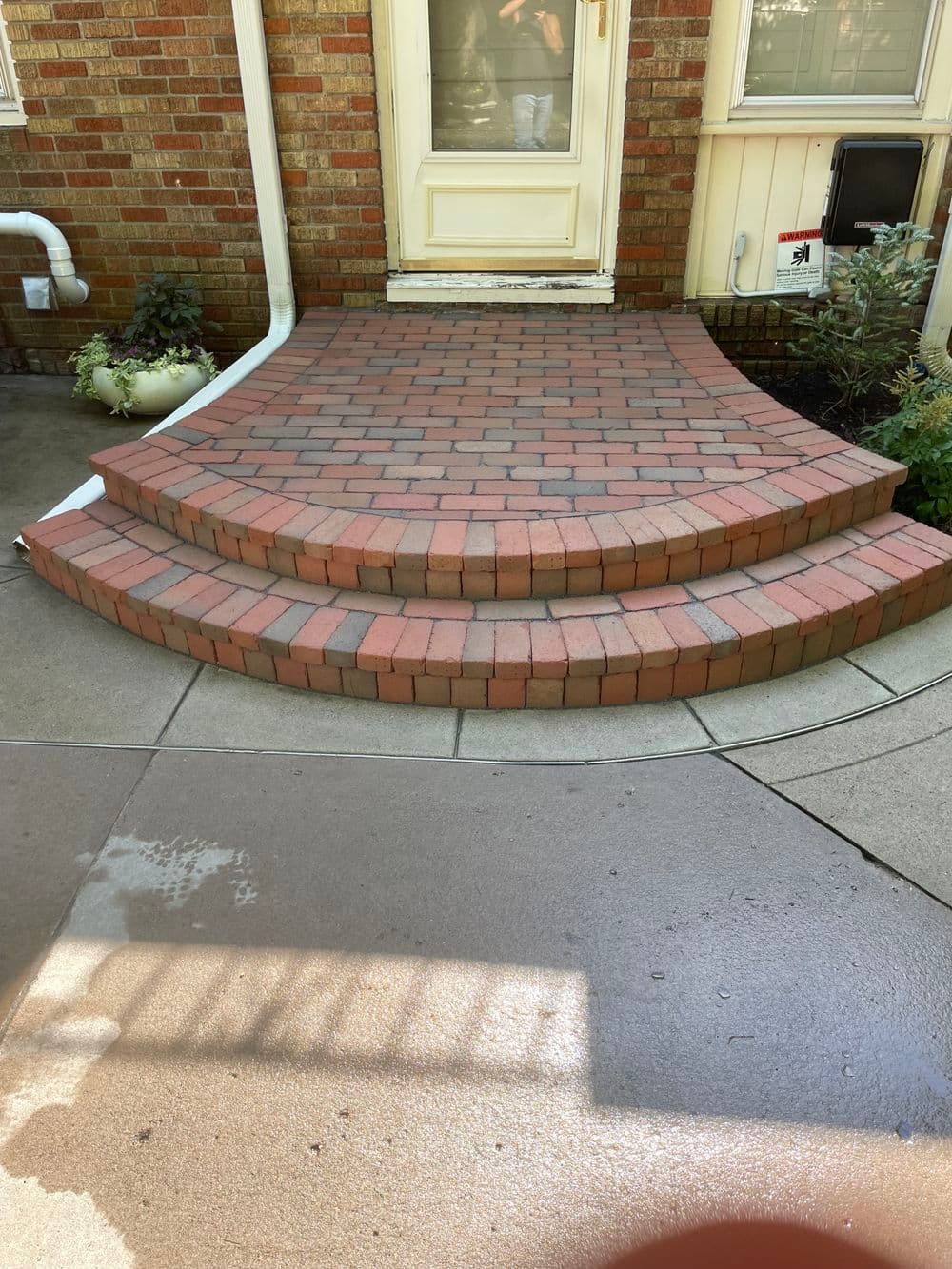 Brick pathway with steps leading to a home's entrance, featuring a clean concrete area.